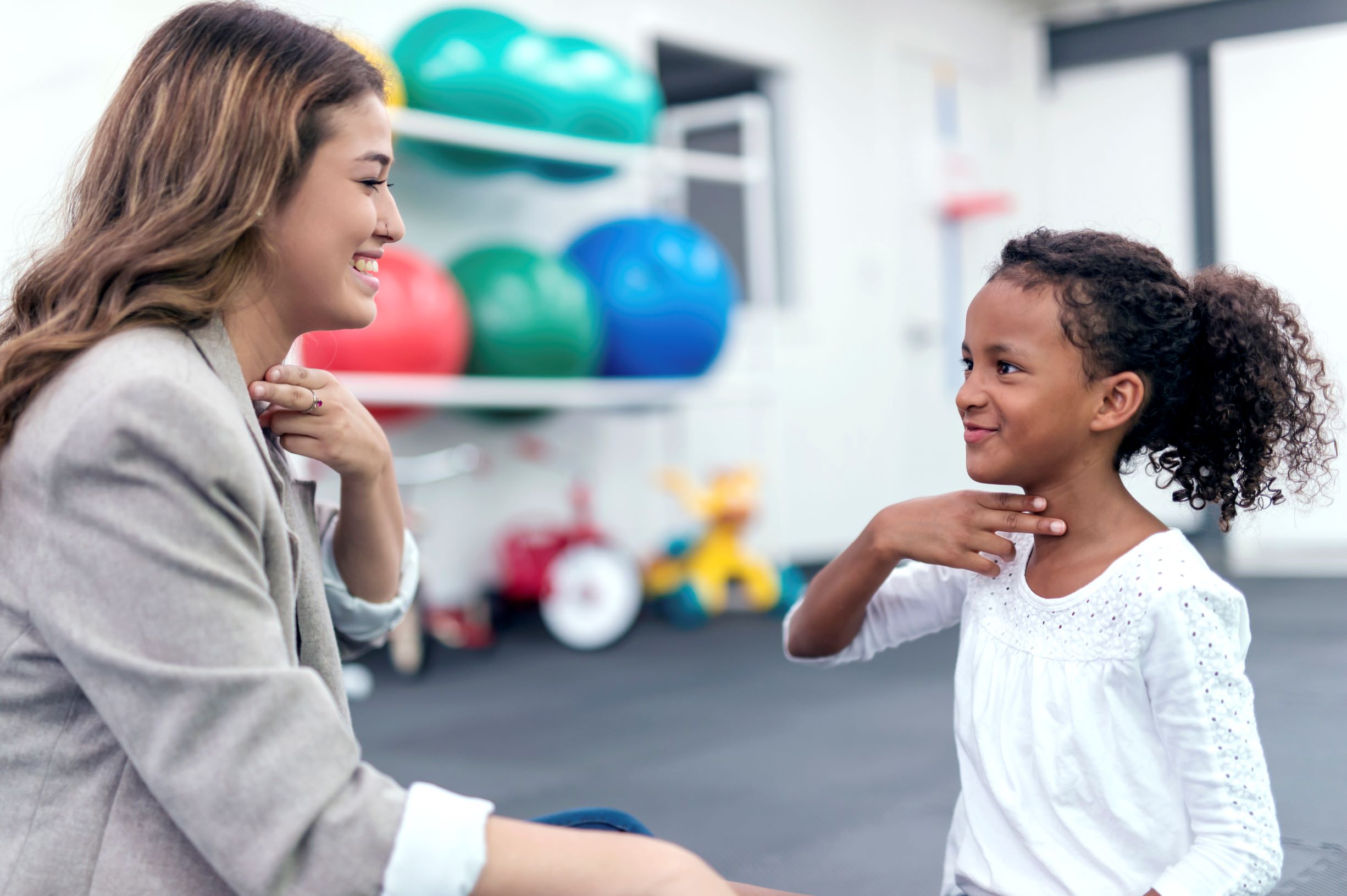 There are many types of speech disorders. In this image, a speech therapist works with a child, who is touching her throat to feel the movements as she makes sounds.