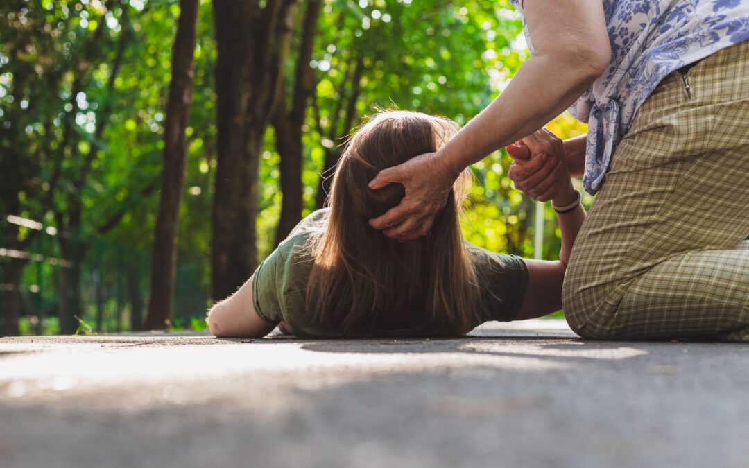 A woman holds a girl's head and hand as she helps her get up off the ground. Although they can be frightening, it's important to understand what to do if someone has a seizure, as well as what not to do.